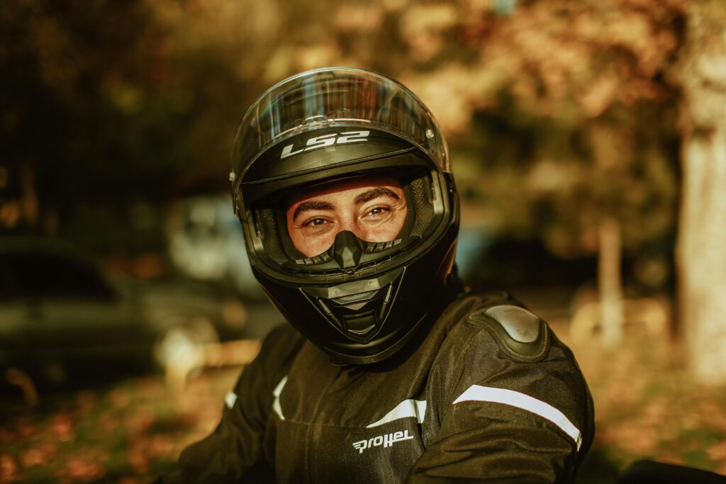 Close-up of a motorcyclist wearing protective gear and helmet outdoors in autumn light.