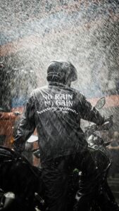 Back view of a motorcyclist riding in heavy rain, wearing a helmet and a jacket with 